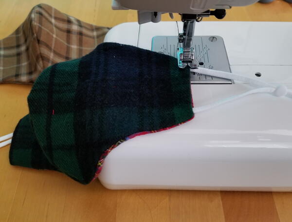 Image shows a sewing machine sewing the earloops onto the flannel fabric face mask.