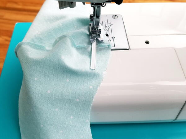 Image shows a machine sewing a nose wire to the mask piece.