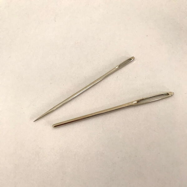 Image shows two tapestry hand sewing needles on a white fabric background.