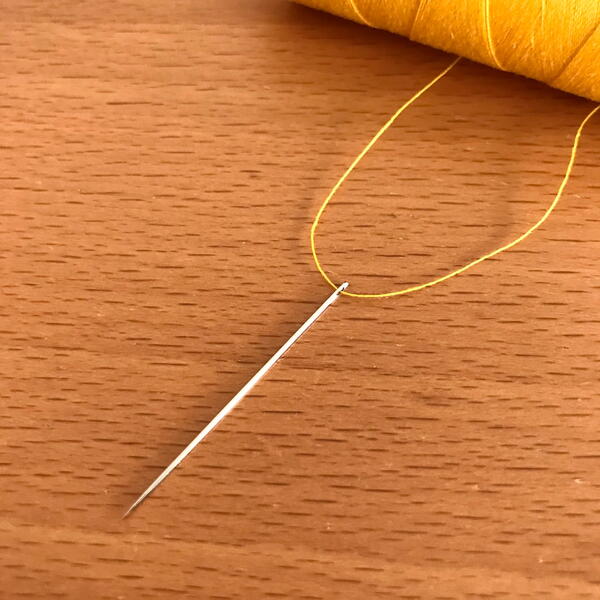 Image shows a threaded hand sewing needle on a wood background.