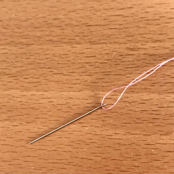 Image shows a threaded hand sewing needle on a wood background.