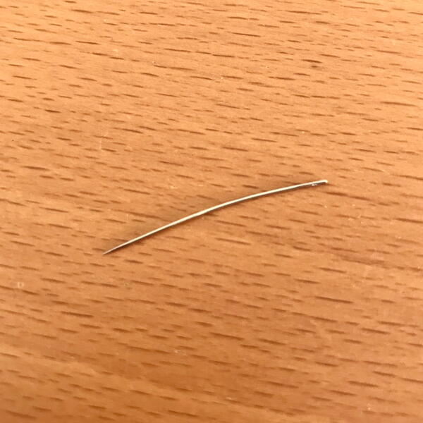 Image shows a bent hand sewing needle on a wood background.