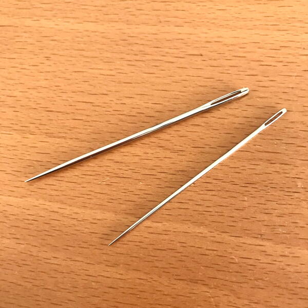 Image shows two darning hand sewing needles on a wood background.