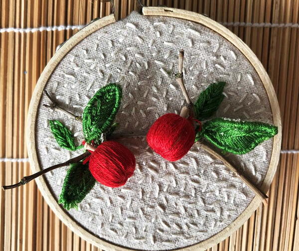 Example of stumpwork embroidery: 3D apples on a white textured background in a wood embroidery hoop.