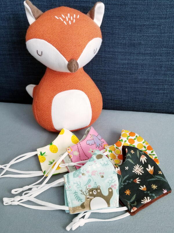 Image shows several finished child size fabric face masks with a fox toy.