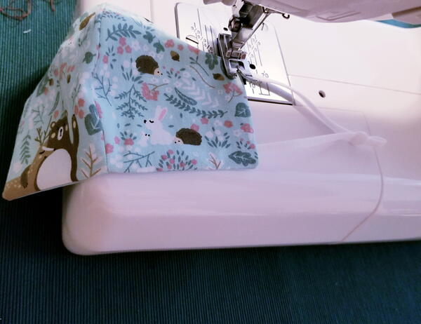 Image shows a sewing machine sewing the earloops onto the child fabric face mask.
