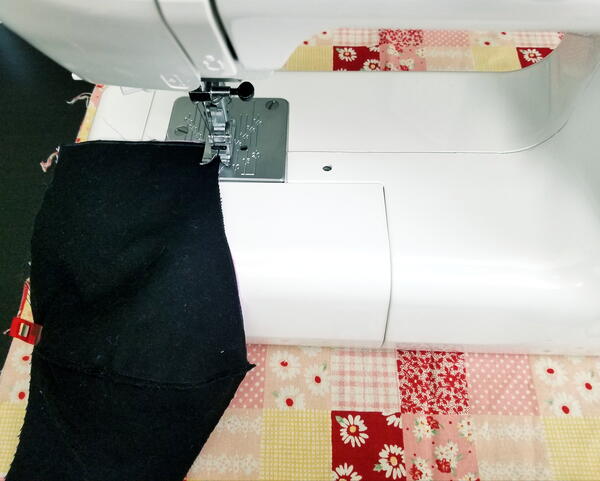 Image shows a sewing machine basting a piece of black fabric.