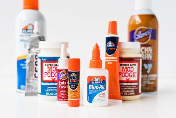 Image shows nine different craft glues set on a table.