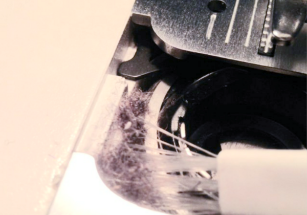 Image shows a small brush cleaning out the hole in a sewing machine where the bobbin sits.