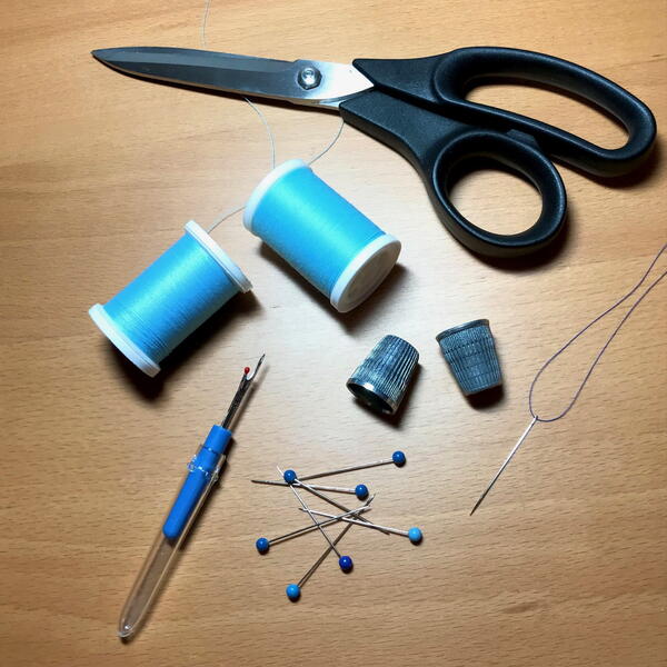 Image shows basic sewing supplies and tools: seam ripper, thread, pins, thimbles, scissors, and a threaded needle