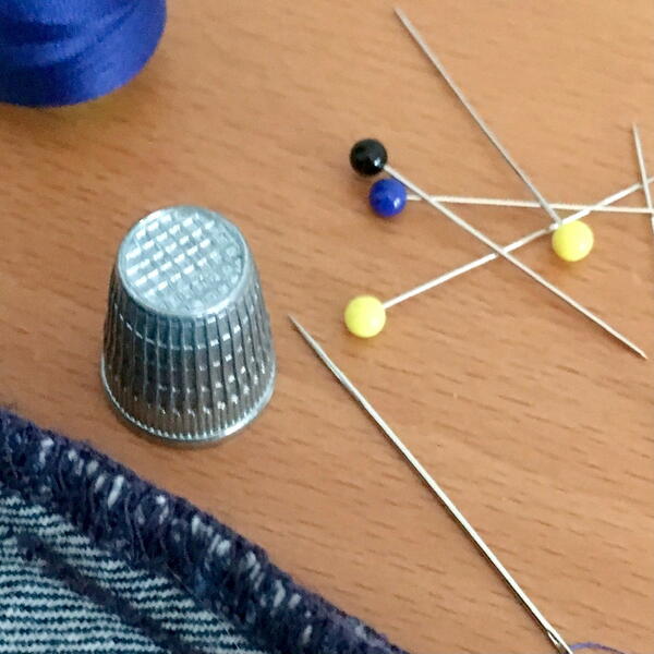 Image shows straight pins and a thimble used in sewing.
