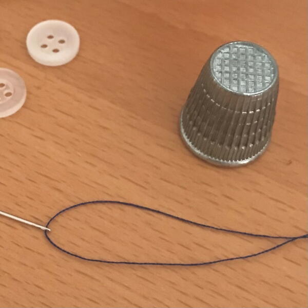 Image shows a thimble, along with a threaded needle and a couple buttons.