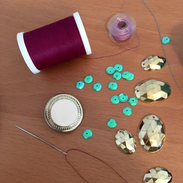 Image shows thread, a threaded needle, sequins, and embellishments.
