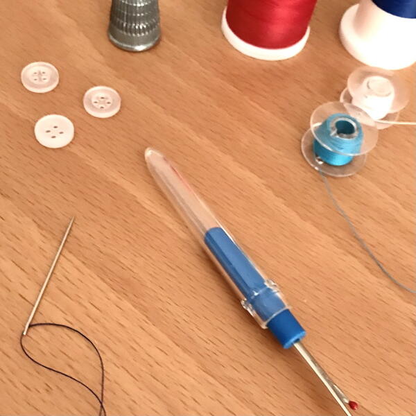 Image shows thread, a threaded needle, seam ripper, buttons, and a thimble.