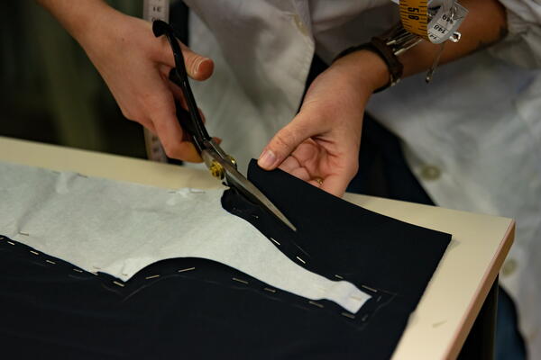 Image shows a person cutting a paper template pinned to fabric on a table with scissors for the difference between fabric scissors and paper scissors.