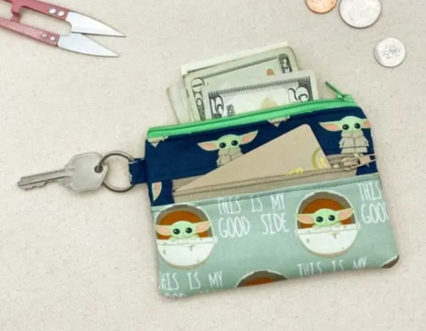 Image shows the Grogu Double Zipper Coin Purse sitting on a table with various items around.