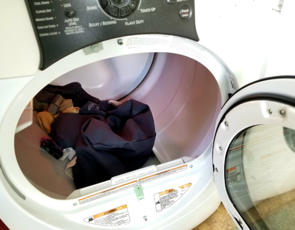 Wash fabrics with like fabrics and colors. Image shows a mix of clothing items in a dryer.