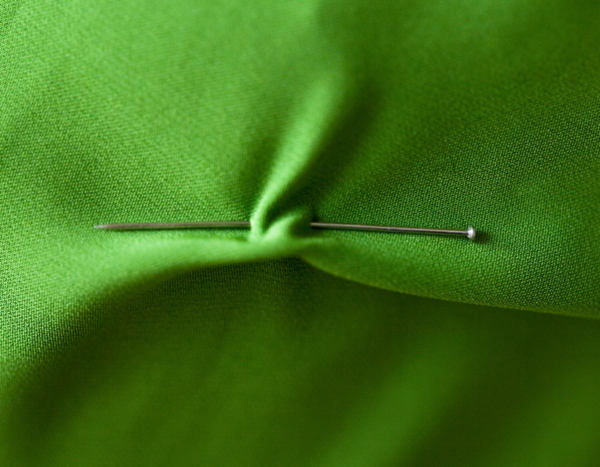 Image shows green fabric puckering from a sewing pin that's pushed through the fabric.