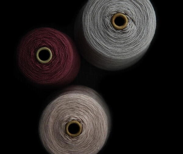 Image shows three large spools of grey, maroon, and beige thead with a black background.