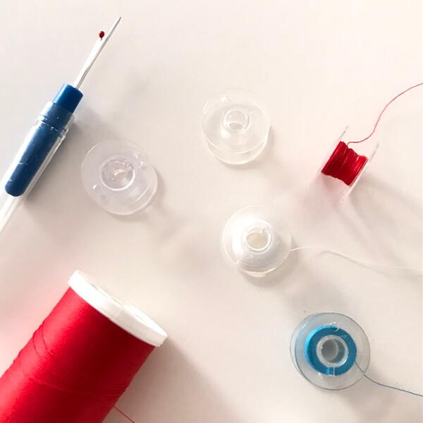 Image shows sewing notions including a seam ripper, spool of thread, and five bobbins with and without thread.