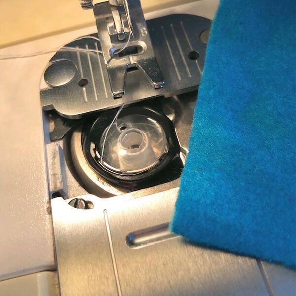 Image shows a bobbin placed inside a sewing machine and a piece of blue fabric on the side.
