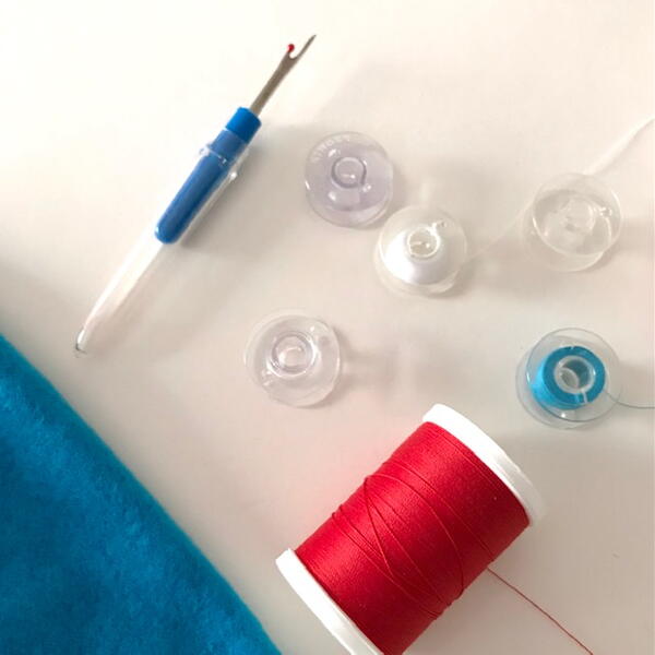 Image shows sewing notions including a seam ripper, spool of thread, and five bobbins with and without thread.