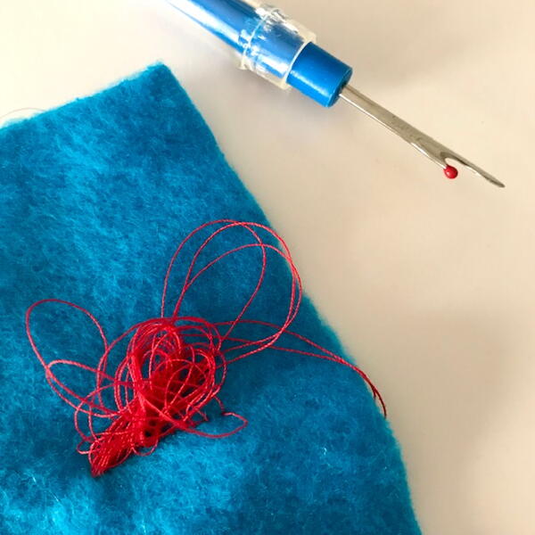 Image shows a seam ripper and a piece of blue fabric with knotted red thread in the center.