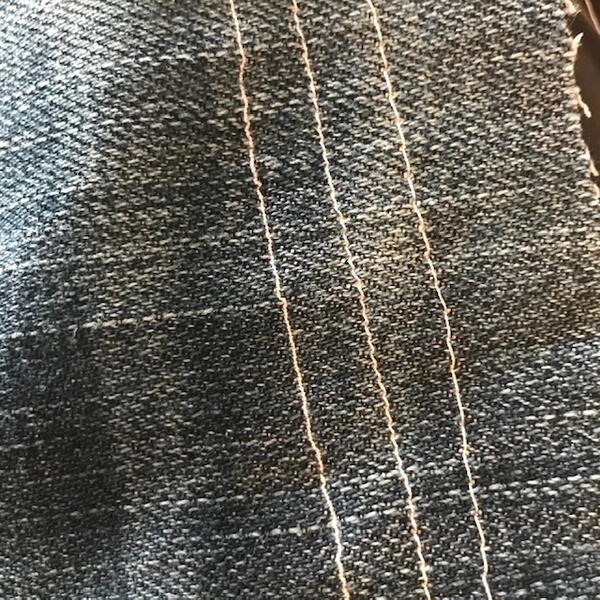 Image is a piece of denim with three long vertical stitches.